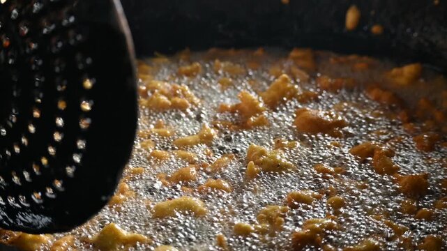 Delicious pakora snack frying deeply in boiling hot oil pan. It is a popular South Asian deep-fried snack made of vegetables, paneer coated in a spiced batter typically composed of gram flour, spices.