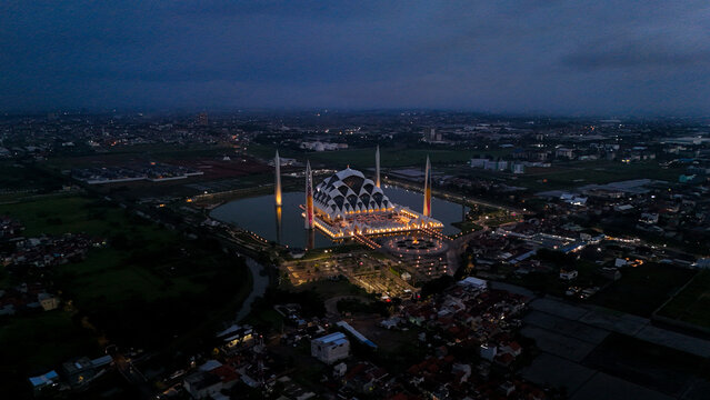 Aerial view of the illuminated Al Jabbar Grand Mosque surrounded by a reflective pond at night in Bandung, West Java, Indonesia.