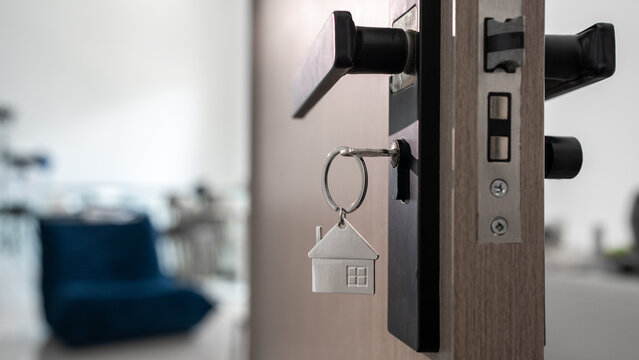 House key with home shaped keychain hanging from a modern door lock, symbolizing home ownership, new property purchase, real estate, moving, security and access to a new residence.