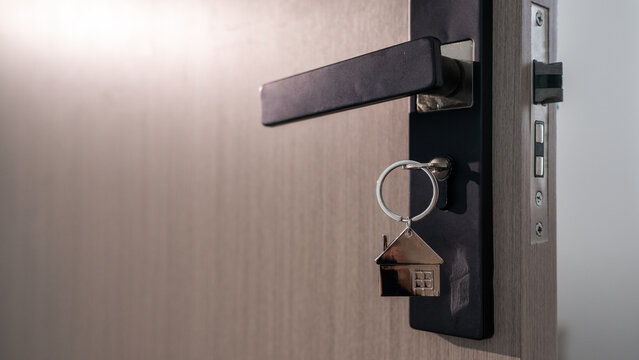 House key with home shaped keychain inserted in a modern door lock, symbolizing home ownership, new property purchase, moving, residential security and access to a new home.
