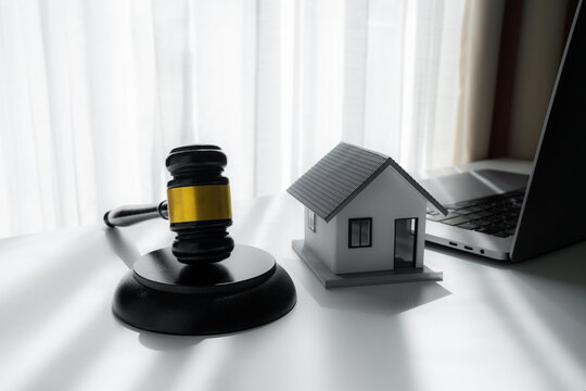 Judge gavel beside a model house and laptop on a desk, representing real estate law, property auction, legal agreement, mortgage dispute, foreclosure and online property transaction.