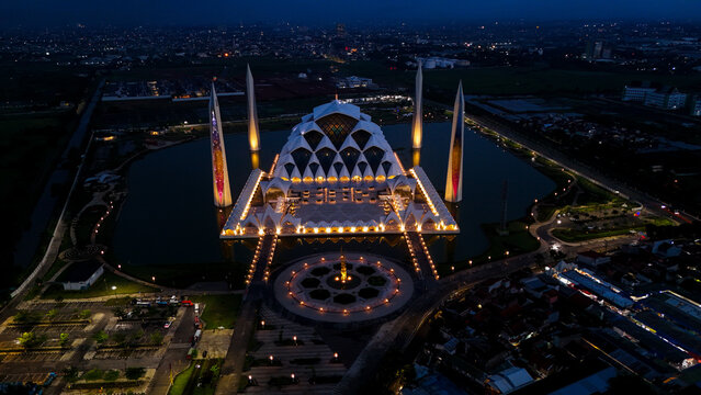 Aerial view of Al Jabbar Grand Mosque illuminated at night, surrounded by a reflective pond and landscaped grounds in Bandung, West Java, Indonesia.