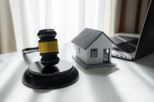 Judge gavel beside a model house and laptop on a desk, representing real estate law, property auction, legal agreement, mortgage dispute, foreclosure and online property transaction.