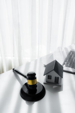 Real estate law concept with judge gavel, model house and laptop on a bright desk with copy space, symbolizing property auction, mortgage foreclosure, legal contracts and housing disputes.