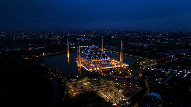 Aerial view of the illuminated Al Jabbar Grand Mosque at night, surrounded by a reflective pond and urban lights in Bandung, West Java, Indonesia.