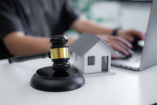 Judge gavel beside house model and person working on laptop symbolizes property law, housing disputes, real estate contracts, mortgage issues, home ownership and online legal consultation.