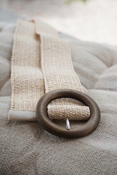 Woven raffia straw belt with round wooden buckle laid on beige linen cushion