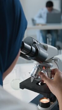 Vertical video of young adult female scientist in hijab adjusting microscope lenses during laboratory research. Footage suits biotechnology, scientific education, pharmaceutical advertising