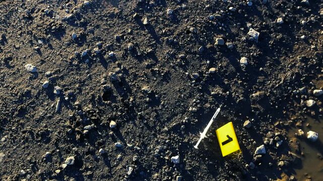 Forensic evidence marker with the number one placed next to a used syringe on muddy ground. A concept for crime scene investigation, drug abuse, overdose death, and law enforcement work