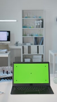 Vertical shot of laptop displaying chroma key green screen standing in research laboratory with test tubes. Footage suitable for biotechnology software mockup and medical digital ads