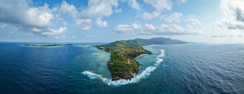 Aerial view of the lush green islands surrounded by turquoise coral reefs and deep blue ocean waters in Karimunjawa, Central Java, Indonesia.