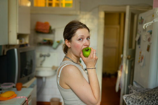 Woman eats an apple in her kitchen