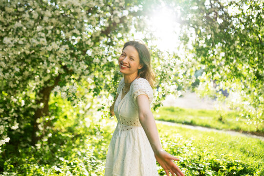 Happy woman enjoys sunny spring day in blooming apple orchard