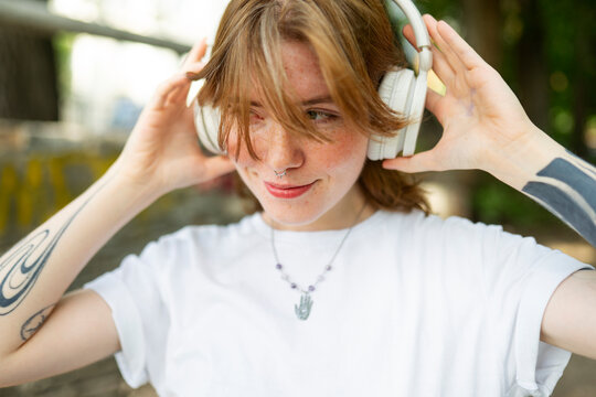 Smiling woman with red hair listens to music outdoors
