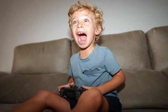 Excited boy screaming while playing a videogame on the sofa indoors
