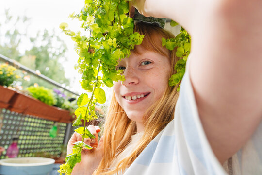 Smiling girl holds a green plant on a balcony enjoying nature
