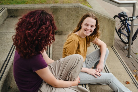 Two teenage girls sitting on stairs outdoors talking and smiling
