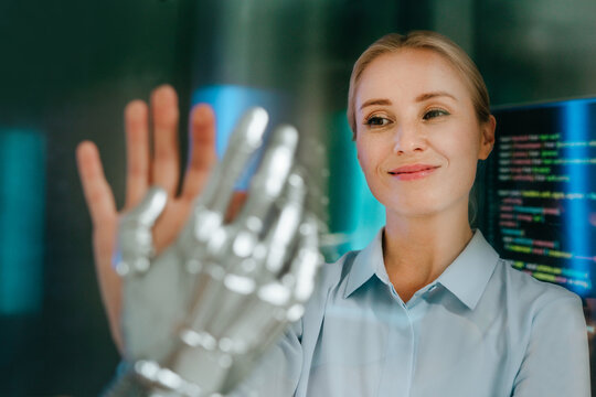 Smiling businesswoman touches a robot hand indoors