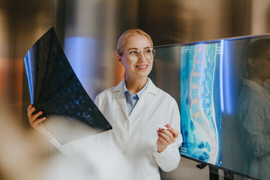 Smiling female doctor holds radiograph near digital spine monitor