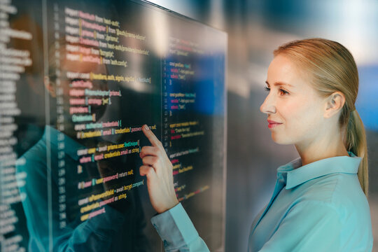 Businesswoman pointing at code on a transparent screen indoors