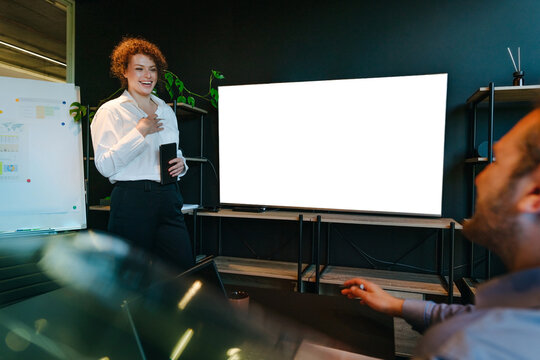 Businesswoman presents to a businessman near a blank screen in office