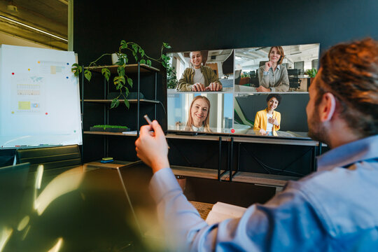 A businessman in an office discusses with colleagues on a video call