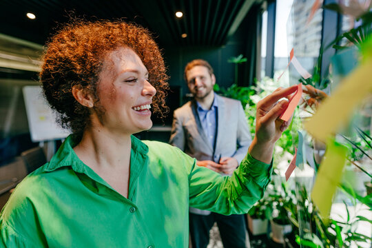 Smiling businesswoman puts note on glass wall in the office