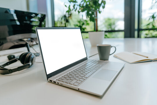 A modern laptop with a blank screen sits on an empty office desk