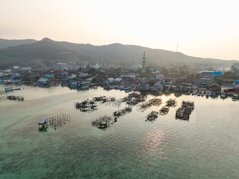 Aerial view of Karimunjawa Village with traditional fish farms, wooden boats, and a mosque minaret rising above the coastal houses in Karimunjawa, Central Java, Indonesia.