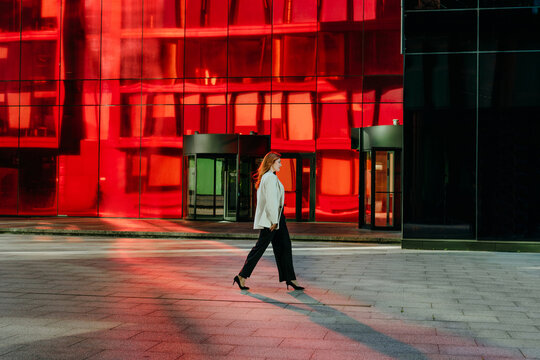 A businesswoman walks past a modern red glass building outdoors