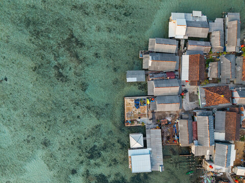 Aerial view of Karimunjawa Village with stilt houses over clear turquoise water, rooftops, and coastal structures in Karimunjawa, Central Java, Indonesia.