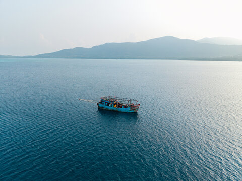 Aerial view of a blue fishing vessel kapal pukat floating on the calm blue sea near the coast of Karimunjawa, Central Java, Indonesia.