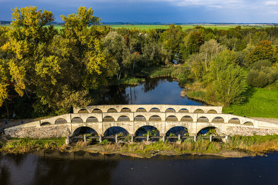 Aerial view of the historic stone arch bridge at Pakruojis Manor surrounded by lush autumn trees and a calm river in Pakruojis, Siauliu apskritis, Lithuania.