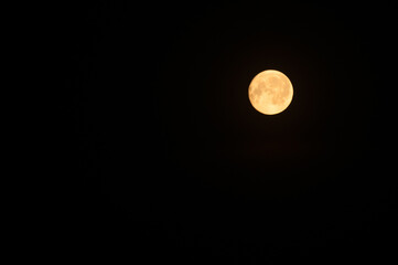 Night sky background with a bright orange full moon glowing against a deep black sky and soft light spreading around the lunar disc © syntheticmessiah