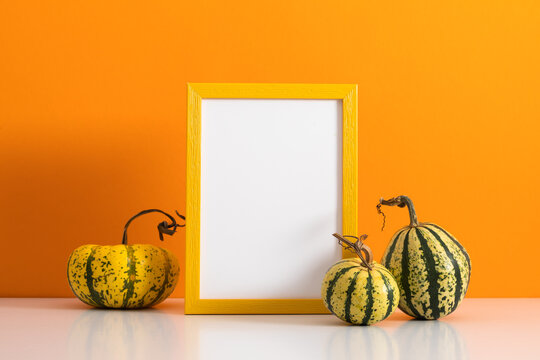 Autumn Thanksgiving mock up frame with green and yellow striped decorative pumpkins on white table. Empty white picture border template for fall season harvest holiday greeting card and promotion.