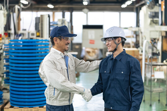 握手する工場作業員。製造業、技能実習生、外国人、人材、雇用、求人、産業、やる気、元気、努力、挑戦