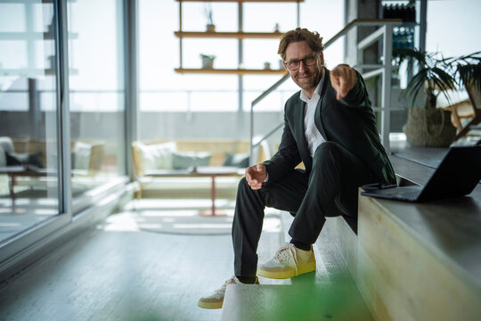 Smiling businessman pointing at camera while sitting on office stairs