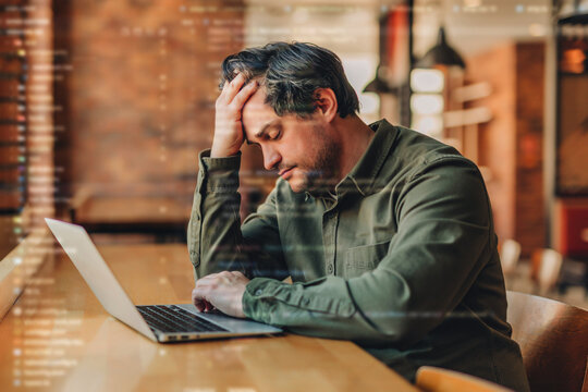Tired businessman works on laptop in modern cafe