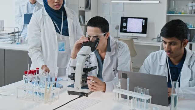 Multiethnic team of scientists analyzing biological samples with microscope and laptop in laboratory. Clip fits biotechnology advertising, medical research and healthcare innovation projects
