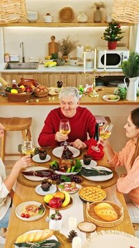 Cheerful family toasting with white wine over a festive homemade feast in a cozy kitchen, surrounded by pies, bread, fruit, and holiday dishes