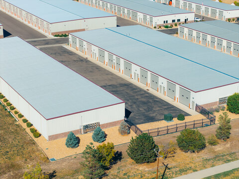 Aerial view of a self storage facility with multiple long warehouse buildings, metal roofs, and paved access lanes in Dacono, Colorado, United States.