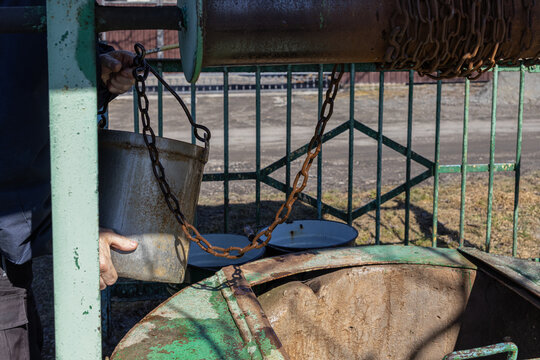A person holds a metal bucket at an old well using a rusty chain to draw water from the underground source, representing rural life, self-sufficiency and traditional resource usage