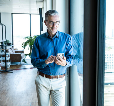 Businessman reads message on smartphone by office window