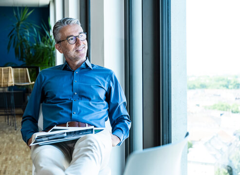 Smiling businessman relaxes by the office window with his device