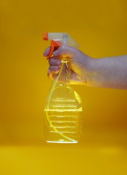 A hand holds a spray bottle with yellow liquid on a yellow background, close-up, subject shooting.