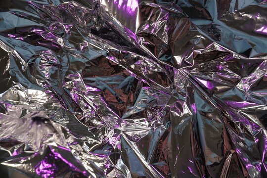 Crumpled aluminum foil with purple reflections. Shiny metallic texture, reflections and folds, silver-violet highlights, abstract background, close-up.