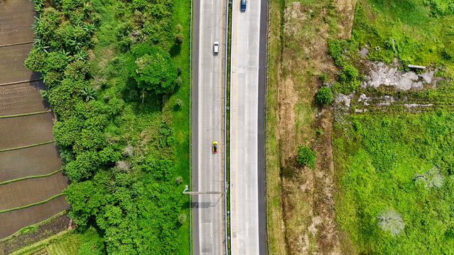 Aerial view of the Soreang-Pasir Koja toll road surrounded by lush rice fields and dense vegetation in Bandung, West Java, Indonesia.