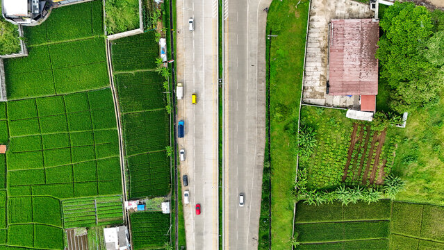Aerial view of the road in Soreang surrounded by lush green rice fields and agricultural plots in Bandung, West Java, Indonesia.