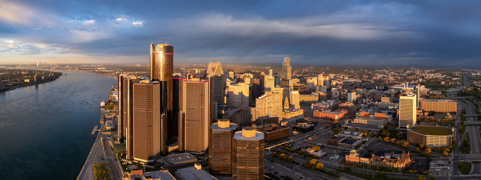 Aerial view of the Downtown Detroit skyline along the Detroit River at sunset, featuring the Renaissance Center and modern skyscrapers under a dramatic cloudy sky in Detroit, Michigan, United States.