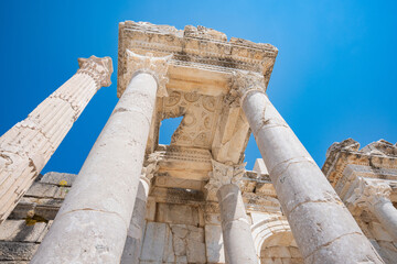 Massive columns rise toward leafy capitals, carved beams, and paneled stonework at Sagalassos archaeological site. Low-angle view © Ensar